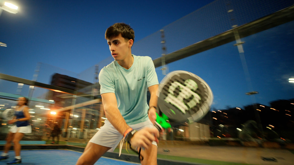 Joueur de padel en revers avec une raquette Black Crown, le soir sur un court